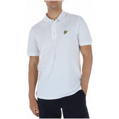 Image 1 : Polo homme Lyle & Scott blanc à manches courtes en piqué coton, aigle brodé doré sur la poitrine, porté avec un pantalon marine — Delvale