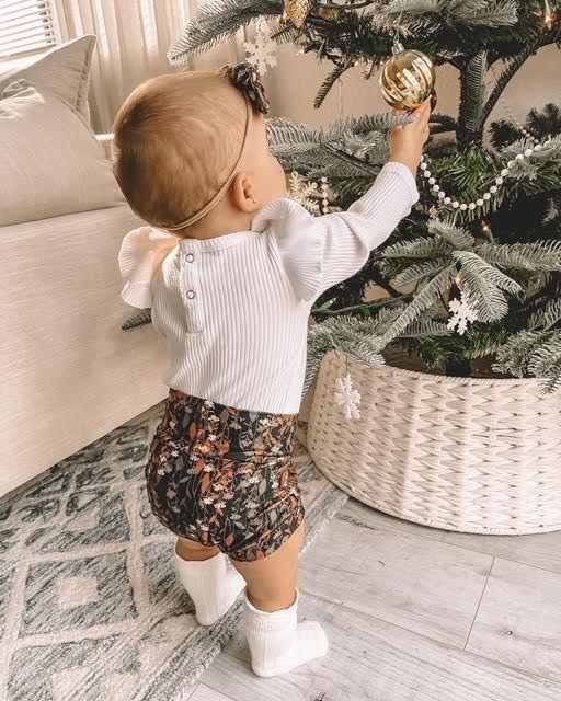 Baby decorating a Christmas tree with ornaments in a cozy living room.