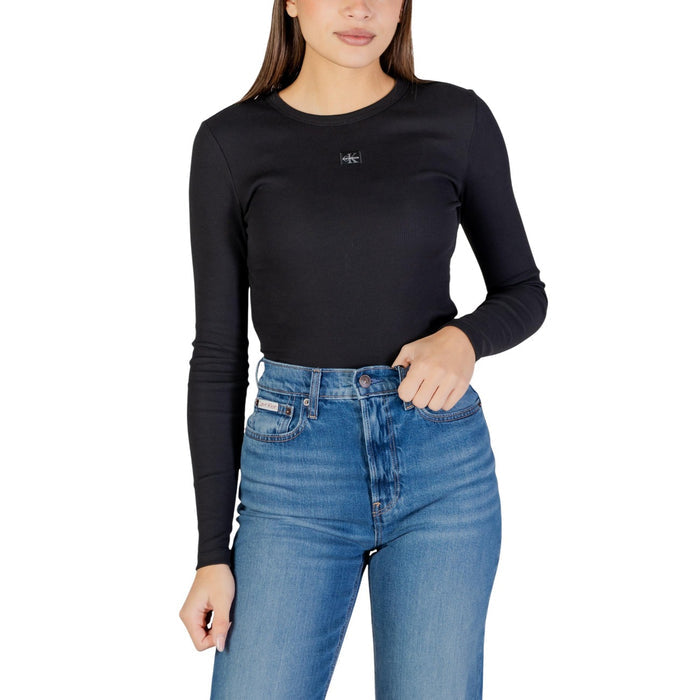 Image 1 : Femme portant un t-shirt noir manches longues côtelé Calvin Klein Jeans avec badge logo CK sur la poitrine, associé à un jean bleu taille haute — Delvale