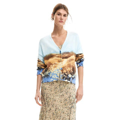 Image 1 : Femme portant le cardigan Desigual à imprimé paysage aquarelle bleu azur et caramel, col en V et boutons dorés, associé à une jupe longue fleurie — Delvale