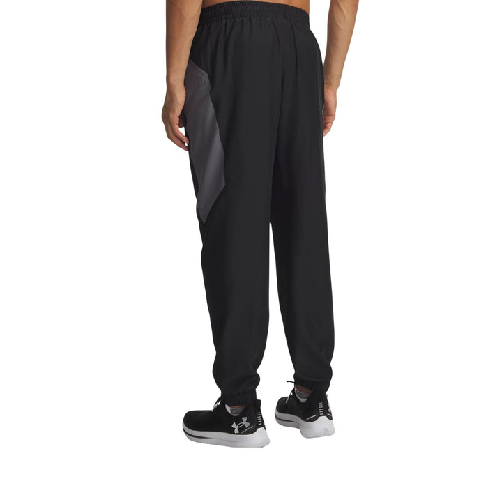 Pantalon technique Under Armour homme noir et gris porté de dos, insert contrasté gris sur les hanches, chevilles élastiquées