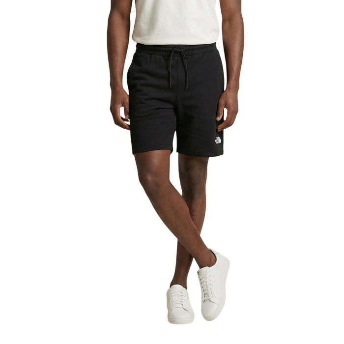 Image 1 : Homme portant un bermuda The North Face noir en coton avec logo brodé blanc sur la cuisse gauche, associé à un t-shirt blanc et des sneakers blanches — Delvale